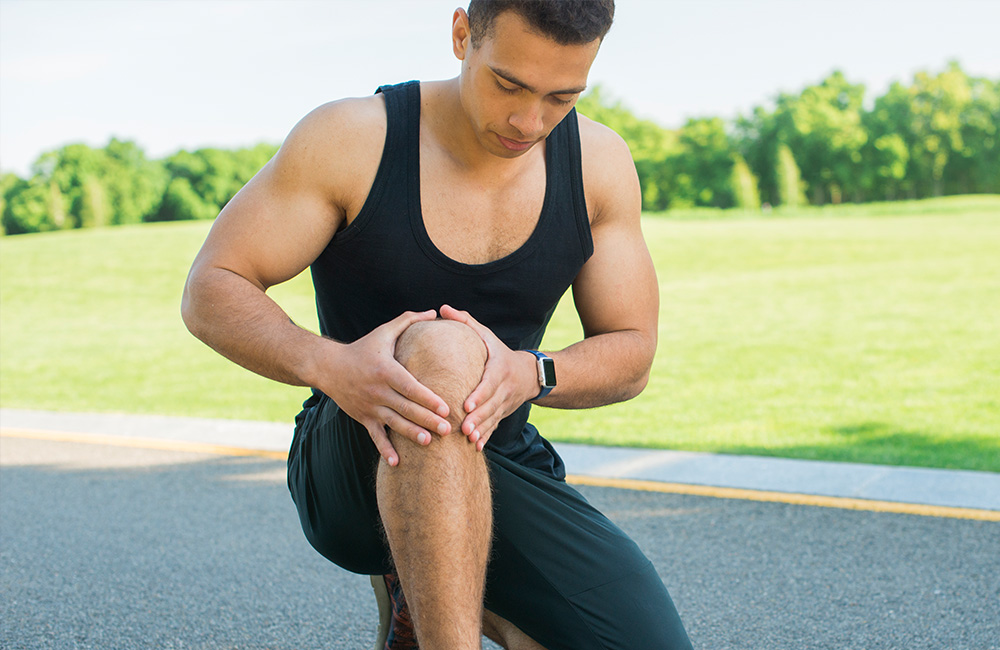 Anwendungsgebiete der Kältetherapie / Neuroreflektorischen Schmerztherapie. Ein junger Mann fässt sich an sein Knie, nach einer Jogging Runde.